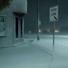 a stop line sign in the middle of a snow covered field at night with street lights behind it