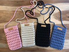 three crocheted purses are lined up on a wooden surface, one is blue and the other is pink