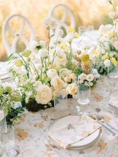 the table is set with white and yellow flowers in vases, silverware, and plates