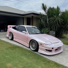 a pink sports car parked in front of a house with palm trees and grass around it