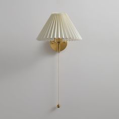 a wall lamp with a white shade hanging from it's side on the wall