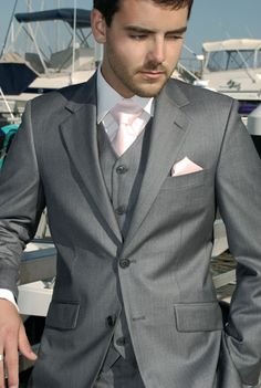 a man in a gray suit and pink tie standing next to a white boat on the water