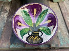 a colorful flower painted on the side of a wooden bowl sitting on top of a piece of wood