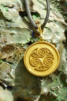 a gold pendant with an intricate design on a black leather cord hanging from a rock