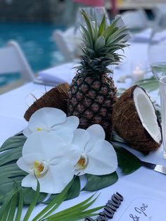 a pineapple, coconuts and flowers are on a table by the pool at a wedding reception