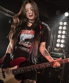 a woman with long hair holding a bass guitar in front of some stage lights and sound equipment