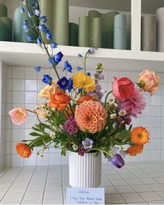 a white vase filled with lots of colorful flowers on top of a counter next to shelves