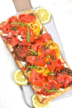 a long piece of bread with tomatoes and herbs on it next to lemon wedges