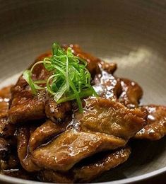 a bowl filled with meat covered in sauce and garnished with green onions on top