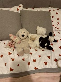 two stuffed animals laying on top of a bed next to pillows with hearts all over them