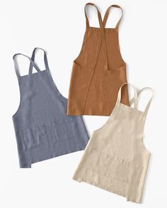 three aprons are lined up next to each other on a white surface, one is blue and the other has brown