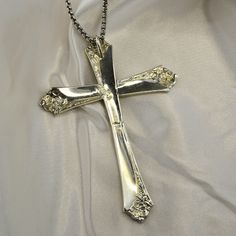 a silver cross on a chain is laying on a white cloth with an intricate design