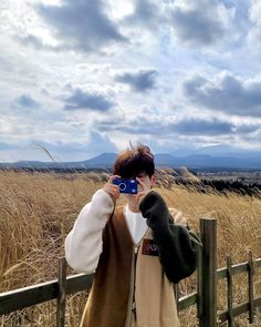 a woman standing in front of a wooden fence holding a cell phone up to her face