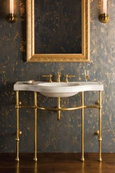 a bathroom sink sitting under a mirror next to a gold framed wall mounted art piece