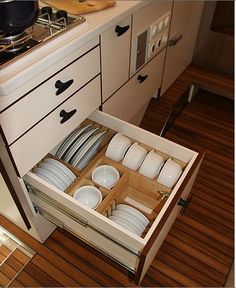 an open drawer in the middle of a kitchen with plates and bowls inside on it