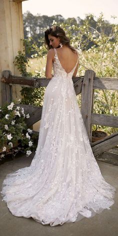 a woman in a white wedding dress standing on a wooden fence with her back to the camera