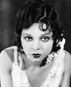 an old photo of a woman with black lips and pearls on her dress, posing for the camera