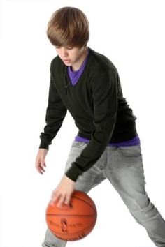 a young boy holding a basketball in his right hand while standing next to a white background