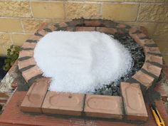 a brick fire pit filled with snow next to a planter and some bricks on the ground