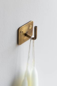 two white vases are hanging on the wall next to a brass hook with an object in it