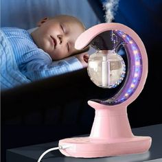 a baby sleeping on top of a table next to a fan with steam coming out of it