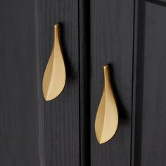 two gold leaf shaped handles on black cupboards with wood grained doors in the background