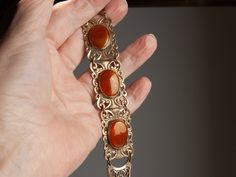 I believe this beautiful bracelet was made in the 1930s. The brass is a rich, gold color and perfectly sets off the caramel-colored oval stones.  The brass panels have a nice weight to them.  The stones could possibly be semi-precious... perhaps brown hematite.   I do see subtle striations.  However, I'll assume they are glass, as I don't have testing equipment.  Also, the photos make them seem a little reddish; they are not.  Caramel brown is more accurate ;-)). This bracelet is in excellent vi Gold Oval Bohemian Bracelets, Bohemian Gold Oval Bracelets, Vintage Bronze Bracelet For Formal Occasions, Antique Brown Bracelet Gift, Vintage Bronze Bracelets For Formal Occasions, Antique Brown Bracelet Ideal For Gifts, Vintage Brown Hallmarked Jewelry, Antique Oval Gold Bracelet, Vintage Cabochon Bracelets