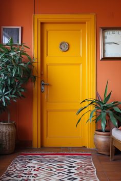 a bright yellow door in an orange room with potted plants next to it and a clock on the wall