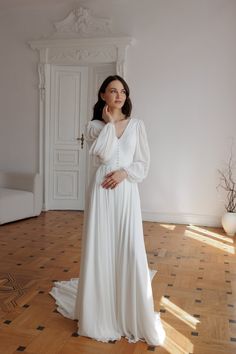 a woman in a white dress standing on a wooden floor with her hands behind her head