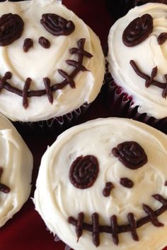 four cupcakes with white frosting and chocolate sprinkles decorated to look like faces