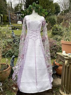 "FASHIONED FROM  A  LUXURIOUS TRULEY GORGEOUS LILAC CRUSHED VELVET  (CONTAINING LYRCA) ...     IDEAL FOR  A  MEDIEVAL / RENAISSANCE THEMED BALL, PARTIES, summer jousts, HANDFASTINGS / WEDDINGS, OR ANY SPECIAL, SACRED OCCASSION, FOR THAT EXTRA WOW FACTOR     THE FRONT PANEL HAS BEEN FASHIONED FROM A TRULY GORGEOUS STUNNING AND UNIQUE WHITE JACQUARD WITH A BEAUTIFUL PALE LILAC  EMBROIDERED DELICATE SCROLL LEAF DESIGN  THE  FULL LENGTH MEDIEVAL  CAPE SLEEVES HAVE  BEEN FASHIONED FROM A LUXURIOUS TR Gothic Purple Wedding Dress, Celtic Bride, Handfasting Dress, Medieval Cape, Lilac Fairy, Wedding Handfasting, Pagan Wedding, Wedding Gown Dress, Handfasting Wedding