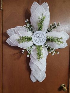 a cross made out of white lace and greenery on a wooden door with the words peace is near it