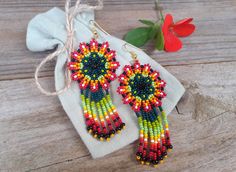 a pair of colorful beaded earrings sitting on top of a wooden table next to a red flower