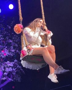 a woman is sitting on a swing with flowers in her hair and holding a microphone