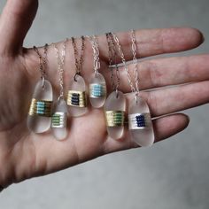 a person's hand is holding five necklaces with different designs on them, all in gold and silver