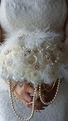 a woman in a wedding dress holding a white bouquet with pearls and feathers on it