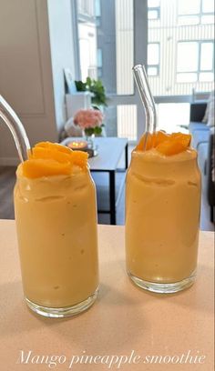 two glasses filled with orange smoothie on top of a table