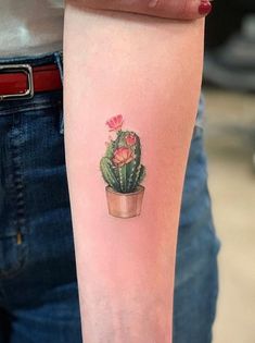 a small cactus tattoo on the left inner arm and wrist, with pink flowers in a pot