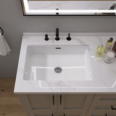 a white sink sitting under a bathroom mirror next to a counter top with bottles on it