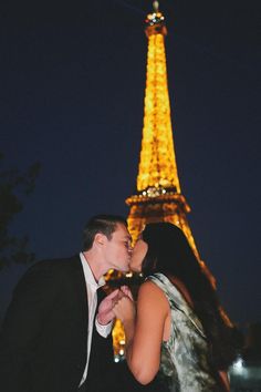 a man and woman kissing in front of the eiffel tower at night time