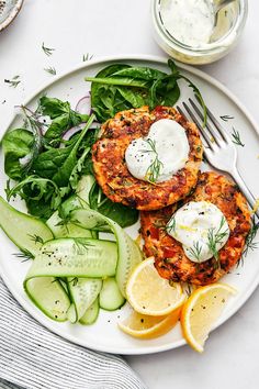 two crab cakes on a plate with cucumbers and lemon wedges next to it