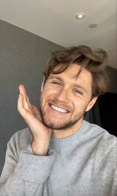 a man smiling and holding his hand up in the air while wearing a gray sweater