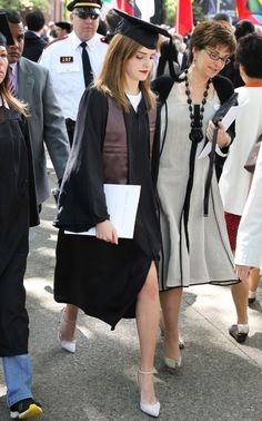 two women in graduation gowns and hats walk down the street with other people behind them