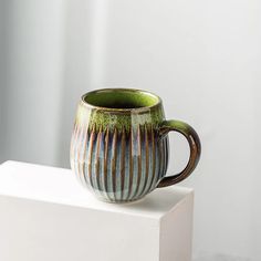 a green and brown coffee cup sitting on top of a white block in front of a window