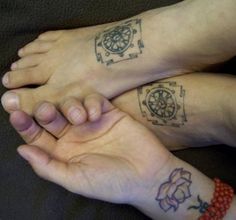 two people with tattoos on their feet sitting next to each other and holding hands together