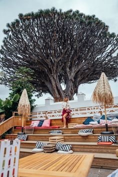 a woman sitting on top of wooden steps next to a large tree with lots of umbrellas