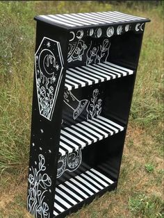 a black and white shelf with drawings on it in the middle of a grassy field