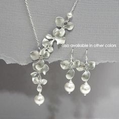 two silver necklaces with flowers and pearls hanging from the back of each one, on a gray background