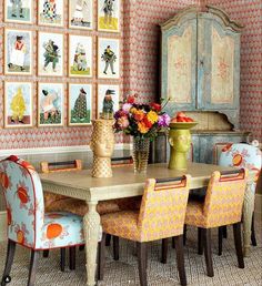 a dining room table with colorful chairs and pictures on the wall behind it in an eclectic style