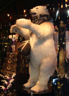 a white polar bear standing on its hind legs in front of a display case filled with suitcases